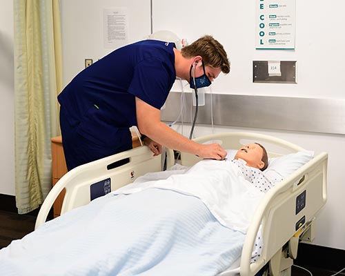 Healthcare student treating mannequin patient in a hospital bed.