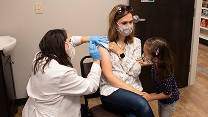 Pharmacist vaccinating a patient with little girl looking on