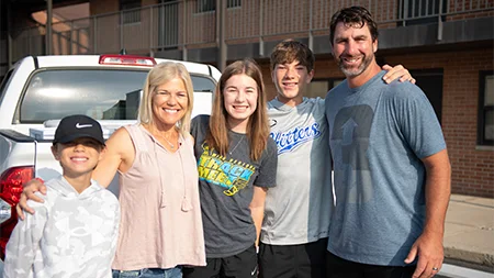 Freshman student smiling with family by dorm.