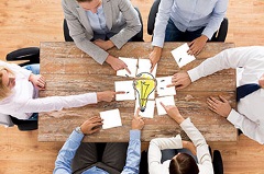 People sitting around a table putting a light bulb  puzzle  together
