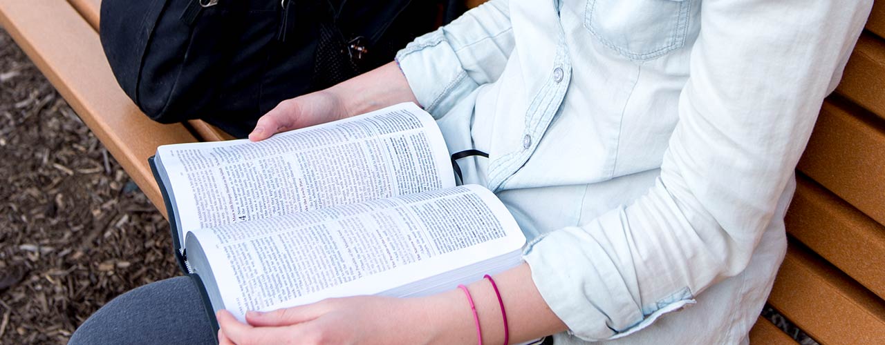 Female student reading her Bible on a park bench