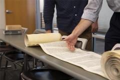 Torahscrollrolledoutontablewithpeoplelookingatit