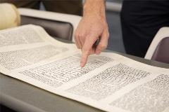 TorahScrollrolledoutontablewithpeoplepointingandanalyzingit
