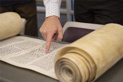 TorahScrollpartiallyrolledoutontablewithpeoplepointingandanalyzingit