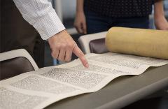 TorahScrollrolledoutontablewithpeoplepointingandanalyzingit