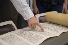 TorahScrollrolledoutontablewithpeoplepointingandanalyzingit