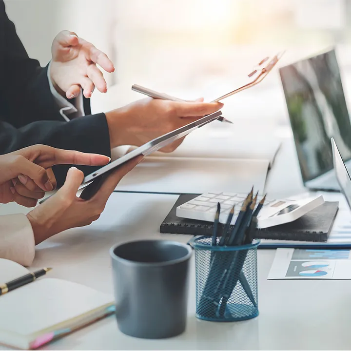 Close-up of business professionals collaborating at a desk with digital tablets, charts, a calculator, and a laptop during a team meeting.